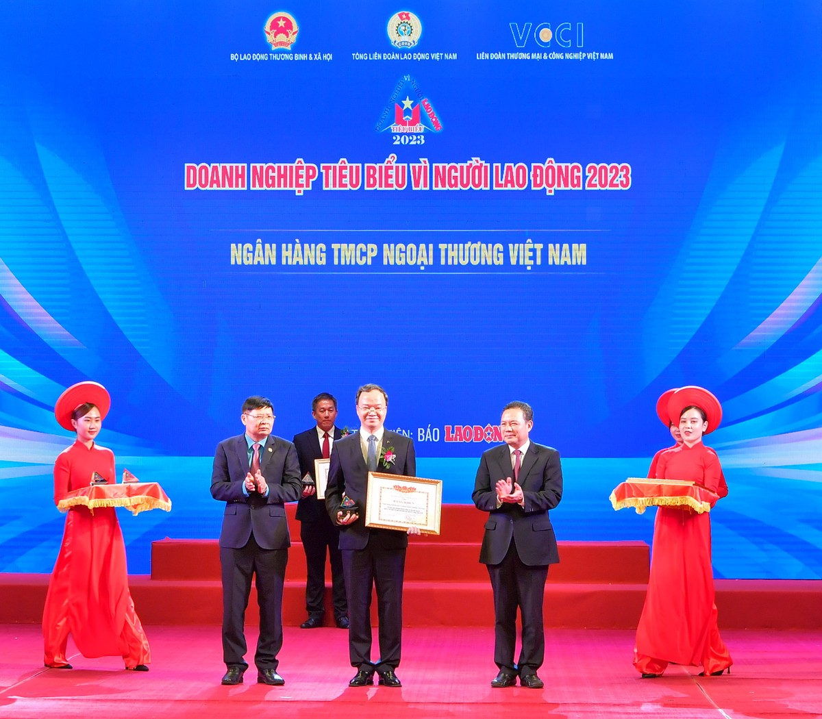 Ông Lê Văn Thanh - Thứ trưởng Bộ Lao động - Thương binh & Xã hội (bên phải) trao Bằng khen “Doanh nghiệp tiêu biểu vì người lao động” và ông Phan Văn Anh - Phó Chủ tịch Tổng Liên đoàn Lao động Việt Nam (bên trái) trao Kỷ niệm chương cho ông Lê Quang Vinh - Phó tổng giám đốc Vietcombank, đại diện Ngân hàng TMCP Ngoại thương Việt Nam tại Lễ vinh danh