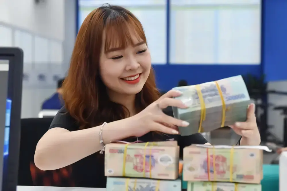 A bank teller counts money at a transaction office in Hà Nội. The credit limit for a customer will be reduced from 15 per cent to 10 per cent in 2029 and for a customer and his/her related parties from 25 per cent to 15 per cent. — Photo cafef.vn