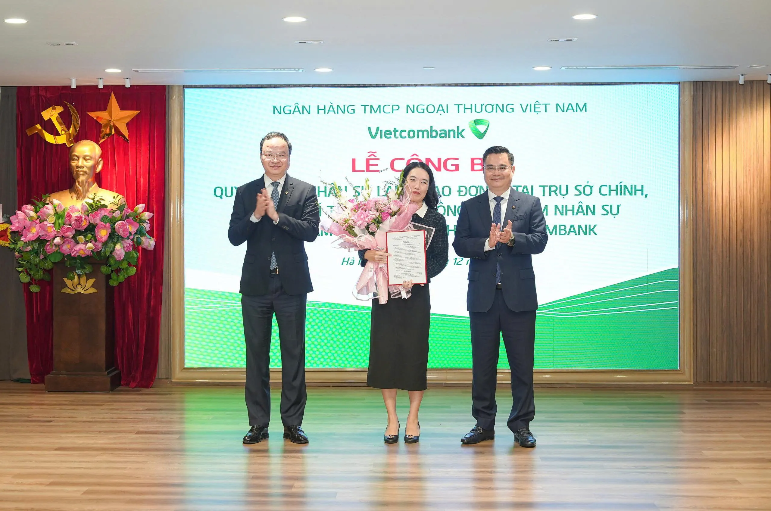 Ông Nguyễn Thanh Tùng - Ủy viên BCH Đảng bộ Chính phủ, Bí thư Đảng ủy, Chủ tịch HĐQT (bên phải) trao quyết định và ông Lê Quang Vinh - Phó Bí thư Đảng ủy, Thành viên HĐQT, Tổng Giám đốc (bên trái) tặng hoa chúc mừng bà Trần Thị Thanh Hoa - Phó Trưởng phòng phụ trách điều hành Phòng Quản lý rủi ro hoạt động Trụ sở chính