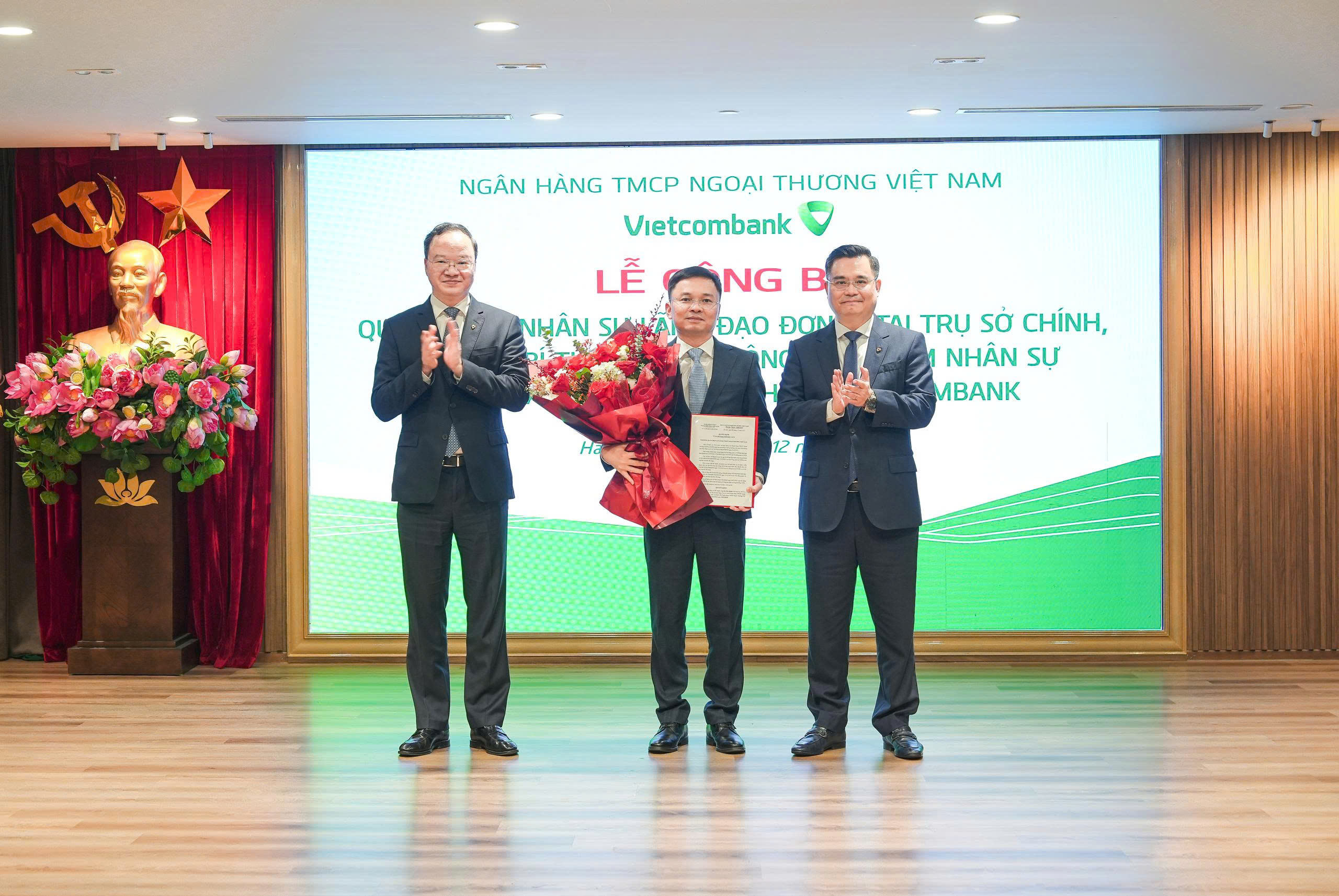 Ông Nguyễn Thanh Tùng - Ủy viên BCH Đảng bộ Chính phủ, Bí thư Đảng ủy, Chủ tịch HĐQT (bên phải) trao quyết định và ông Lê Quang Vinh - Phó Bí thư Đảng ủy, Thành viên HĐQT, Tổng Giám đốc (bên trái) tặng hoa chúc mừng ông Hà Đức Quân - tân Bí thư Chi bộ, Giám đốc Vietcombank Ninh Bình