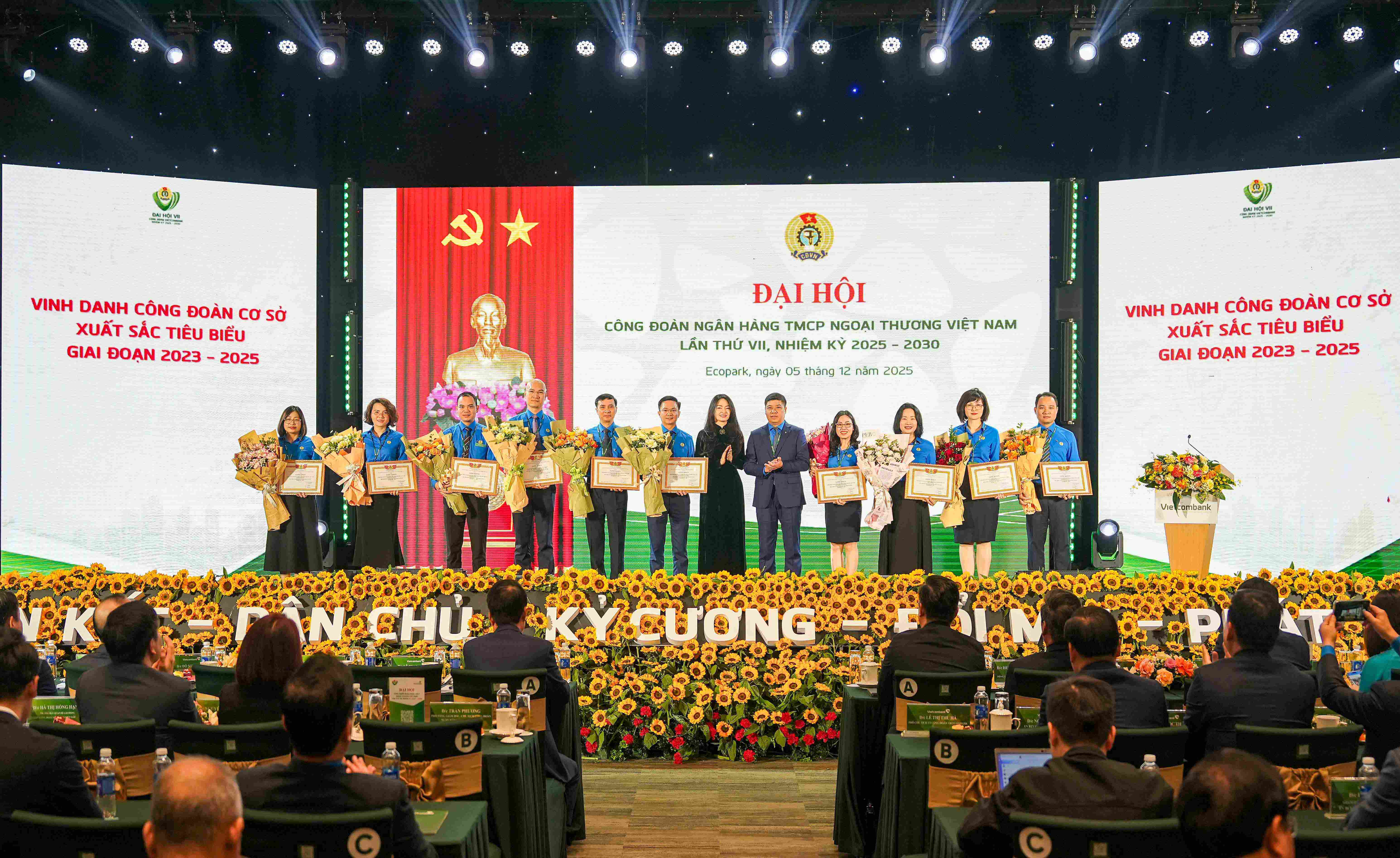 Ông Hồng Quang - Chủ tịch Công đoàn Vietcombank (thứ 5 từ phải sang) và bà Nguyễn Khánh Chi - Phó Chủ tịch Thường trực Công đoàn NHVN (thứ 7 từ trái sang) trao giấy khen và tặng hoa chúc mừng 10 tập thể