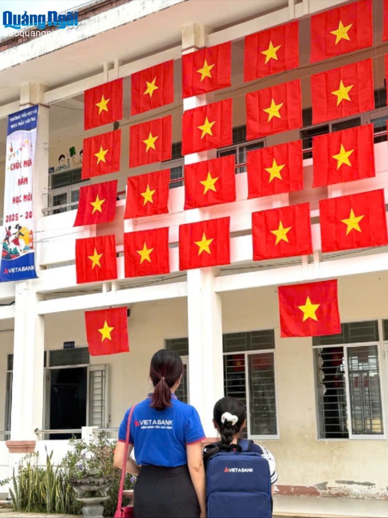 Nhân viên của Ngân hàng TMCP Việt Á - Chi nhánh Quảng Ngãi, cùng học sinh Trường Tiểu học và THCS Trần Văn Trà, xã Tịnh Khê chụp ảnh lưu niệm cùng cờ đỏ, sao vàng và ba lô của ngân hàng.