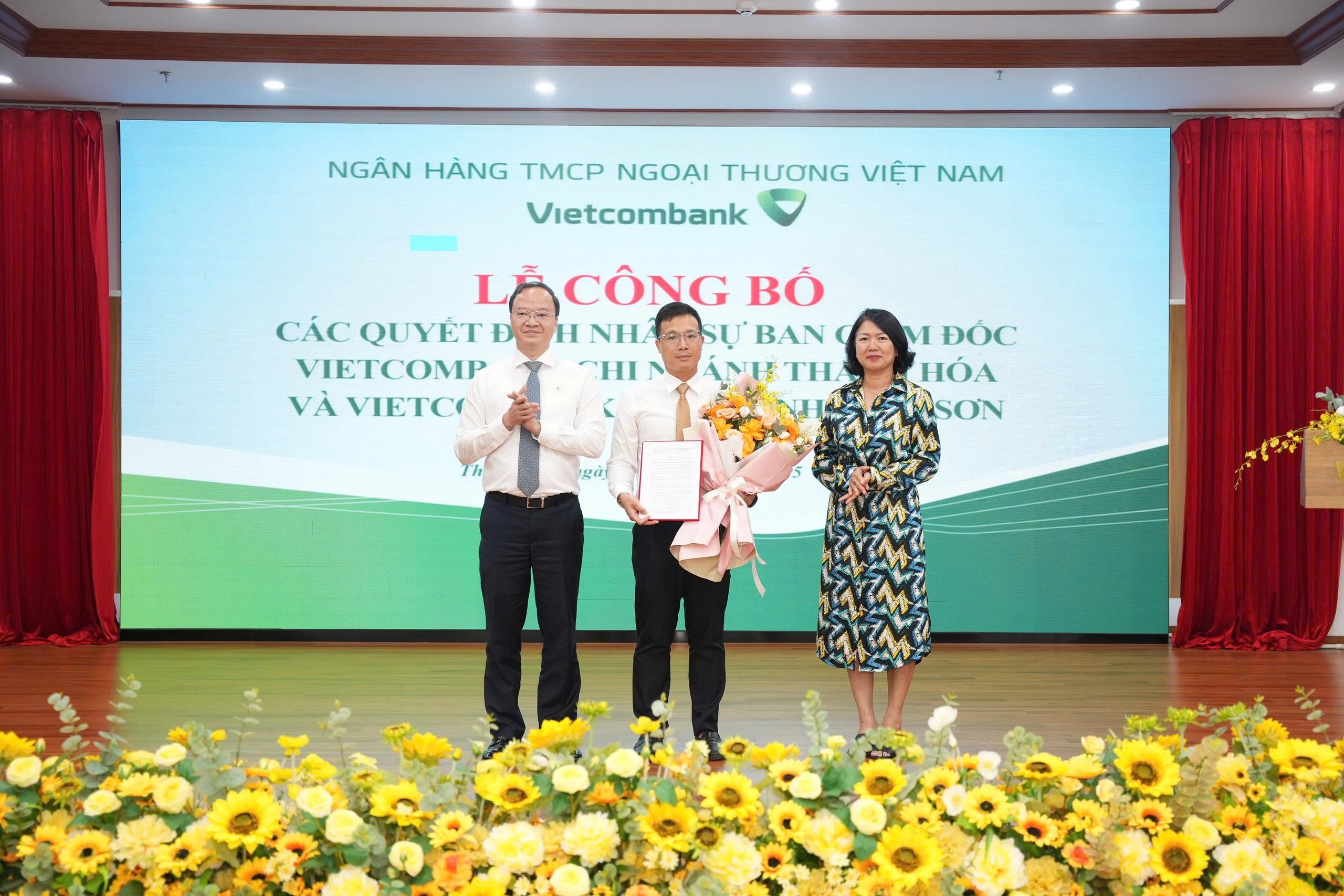 Ông Lê Quang Vinh - Phó Bí thư Đảng ủy, Tổng Giám đốc (bên trái) trao Quyết định và bà Nguyễn Thị Hồng Vân - Giám đốc Khối Pháp chế và Tuân thủ (bên phải) tặng hoa chúc mừng ông Lê Thanh Đức - Phó Giám đốc phụ trách điều hành Vietcombank chi nhánh Nghi Sơn