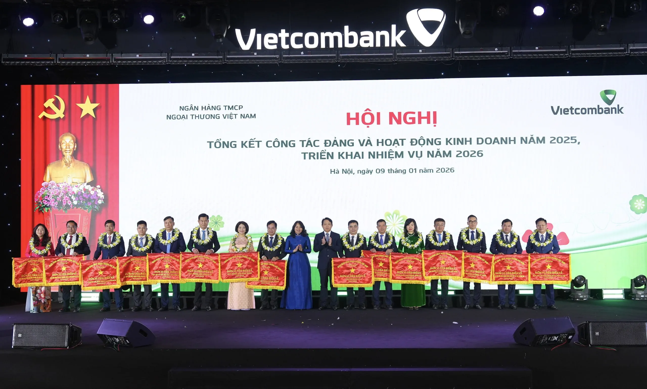 Đ/c Nguyễn Mạnh Hùng - Ủy viên BTV Đảng ủy, Thành viên HĐQT Vietcombank (thứ 10 từ trái sang) và đ/c Đinh Thị Thái - Ủy viên BTV Đảng ủy, Trưởng Ban Kiểm soát Vietcombank (thứ 9 từ trái sang) trao cờ và tặng hoa chúc mừng cho 15 chi nhánh tiêu biểu trong 15 mảng nghiệp vụ quan trọng năm 2025
