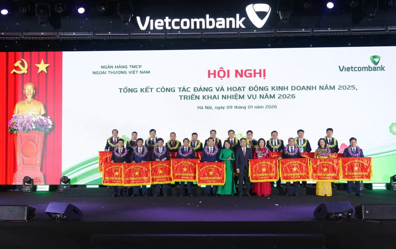 Đ/c Nguyễn Tuấn Anh - Ủy viên BCH Đảng bộ, Thành viên HĐQT Vietcombank (thứ 7 từ trái sang, hàng đầu) và đ/c Hoàng Thanh Nhàn - Ủy viên BCH Đảng bộ, Thành viên HĐQT Vietcombank (thứ 6 từ trái sang, hàng đầu) trao cờ và tặng hoa chúc mừng 19 chi nhánh và 01 công ty con hoàn thành tốt tiêu biểu năm 2025