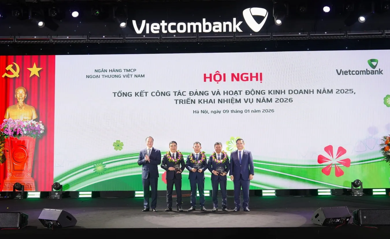 Đ/c Nguyễn Thanh Tùng - Ủy viên BCH Đảng bộ Chính phủ, Bí thư Đảng ủy, Chủ tịch HĐQT Vietcombank (ngoài cùng bên phải) và đ/c Lê Quang Vinh - Phó Bí thư Đảng ủy, Thành viên HĐQT, Tổng Giám đốc Vietcombank (ngoài cùng bên trái) trao biểu trưng và tặng hoa vinh danh cho đại diện 03 đơn vị hoàn thành đặc biệt xuất sắc nhiệm vụ kinh doanh năm 2025 gồm Vietcombank Sở giao dịch, Vietcombank Nam Sài Gòn, Vietcombank Thành Công