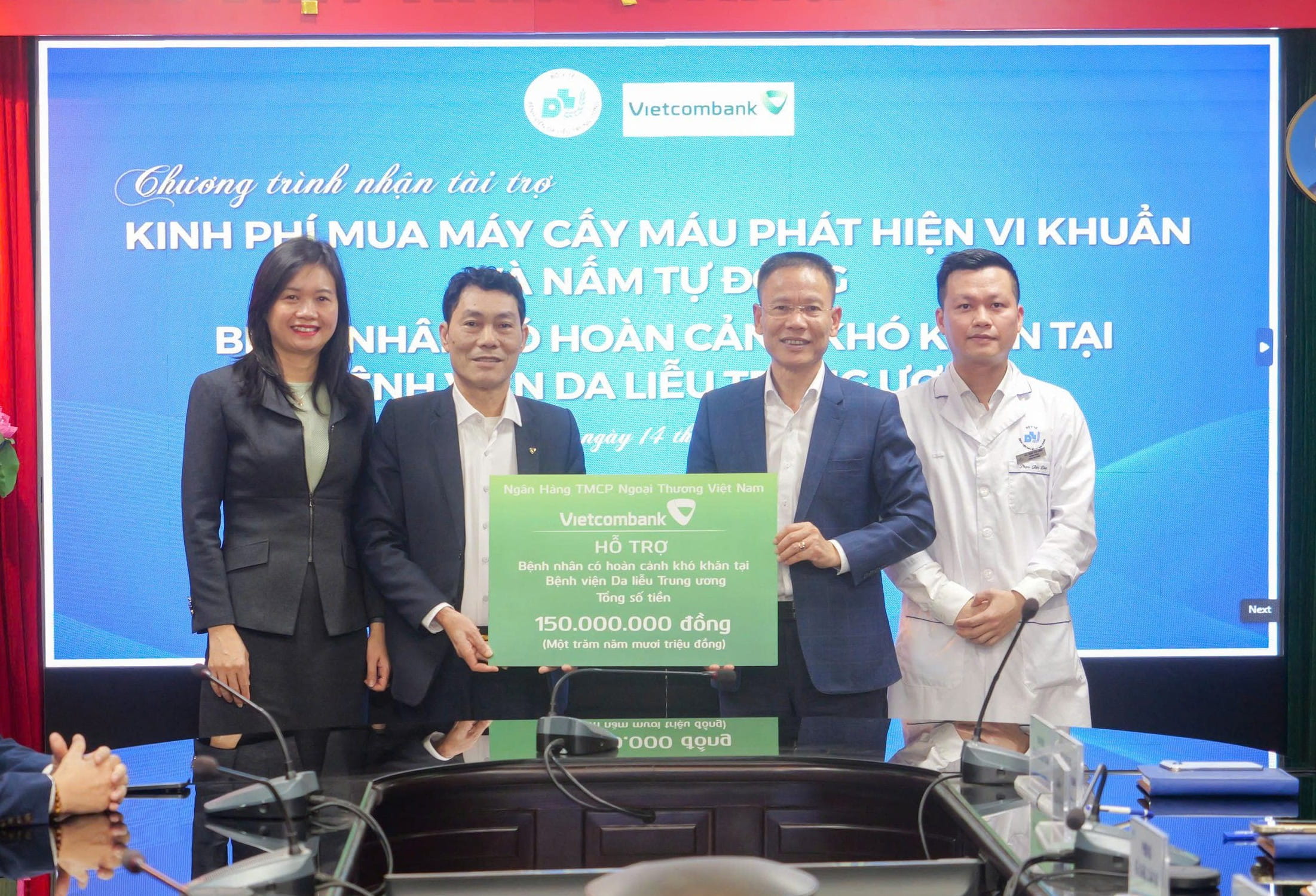 Ông Thái Thăng Long - Giám đốc Vietcombank Nam Hà Nội (thứ 2 từ trái sang) cùng bà Hoàng Thị Khánh - Trưởng phòng Tài chính Kế toán TSC Vietcombank (ngoài cùng bên trái) trao bảng tượng trưng khoản kinh phí của Vietcombank hỗ trợ bệnh nhân có hoàn cảnh khó khăn cho đại diện Bệnh viện là ThS. Phạm Văn Dũng - Trưởng phòng Tài chính Kế toán và ông Phạm Tiến Dũng - phụ trách Phòng Công tác xã hội