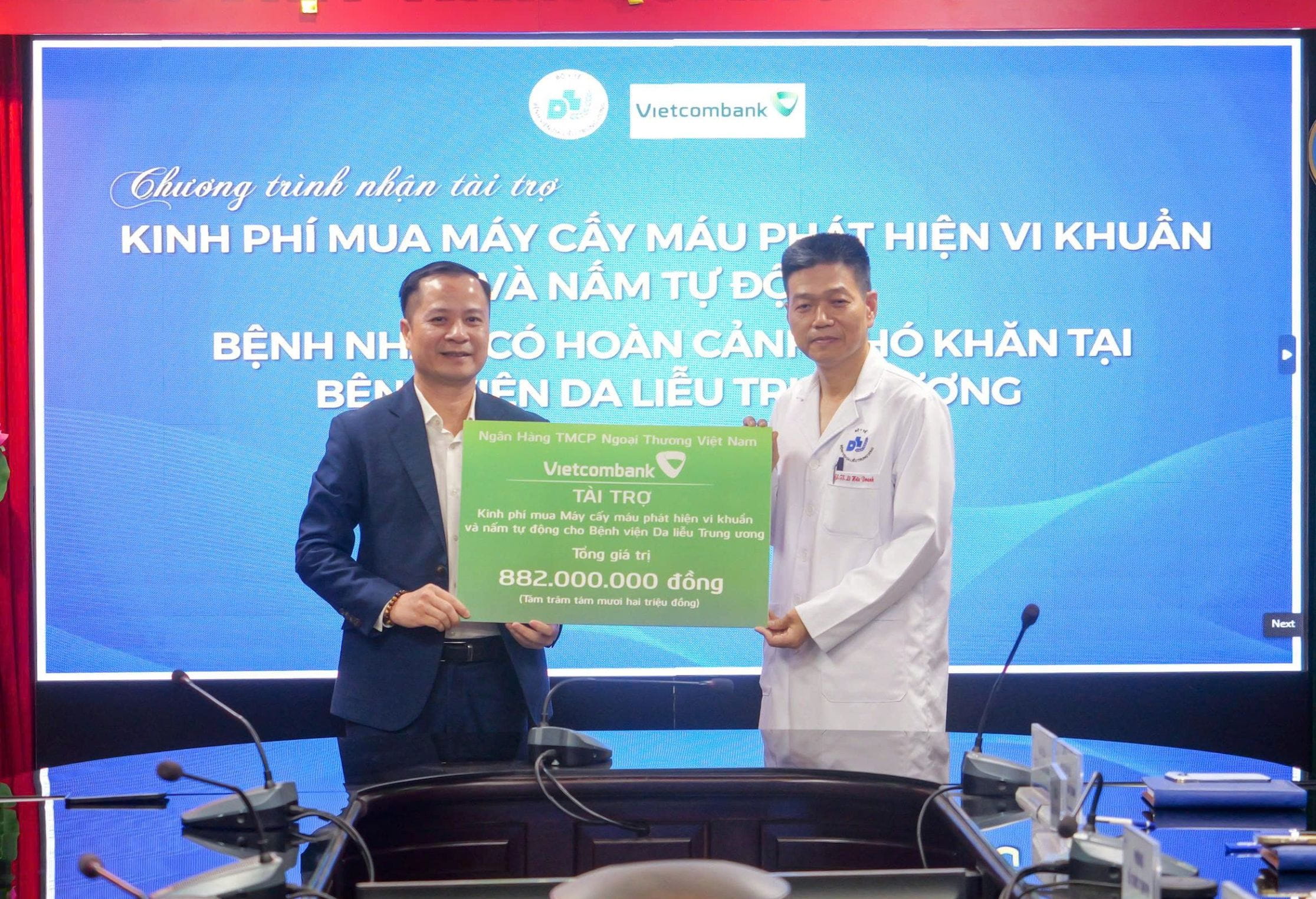 Ông Lê Hoàng Tùng - Phó Tổng Giám đốc (bên trái) trao bảng tượng trưng khoản kinh phí tài trợ của Vietcombank cho đại diện lãnh đạo Bệnh viện Da liễu Trung ương - PGS.TS Lê Hữu Doanh, Bí thư Đảng uỷ, Giám đốc Bệnh viện