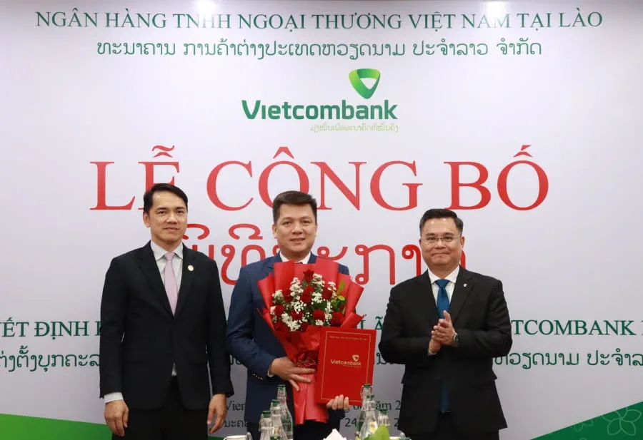 Đ/c Soulysak Thamnuvong - Phó Thống đốc BOL (bên trái) và đ/c Nguyễn Thanh Tùng - Bí thư Đảng ủy, Chủ tịch HĐQT Vietcombank (bên phải) trao quyết định và tặng hoa cho đ/c Hồ Văn Tuấn - Phó Tổng Giám đốc Vietcombank, Chủ tịch HĐQT Vietcombank Lào