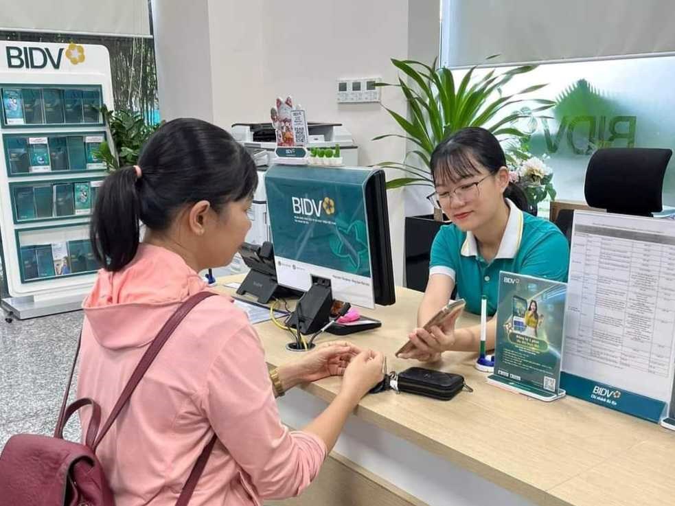 Nhân viên ngân hàng BIDV hỗ trợ khách hàng cài đặt sinh trắc học tại quầy. Ảnh: BNEWS phát