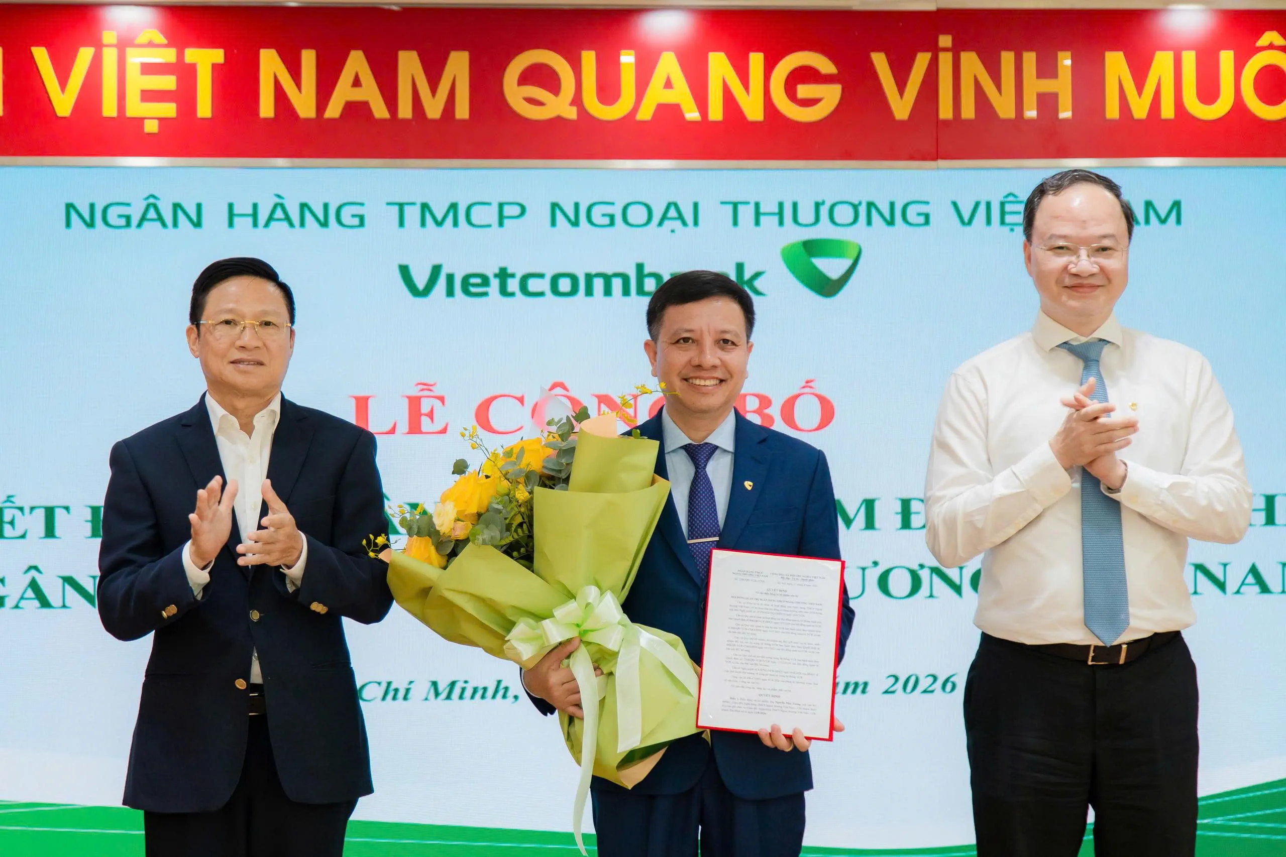 Ông Võ Minh Tuấn - Giám đốc Ngân hàng Nhà nước Khu vực 2 (bên trái) cùng ông Lê Quang Vinh - Thành viên HĐQT, Tổng Giám đốc Vietcombank (bên phải) trao quyết định và tặng hoa chúc mừng ông Nguyễn Như Tưởng - tân Giám đốc Vietcombank Tân Định