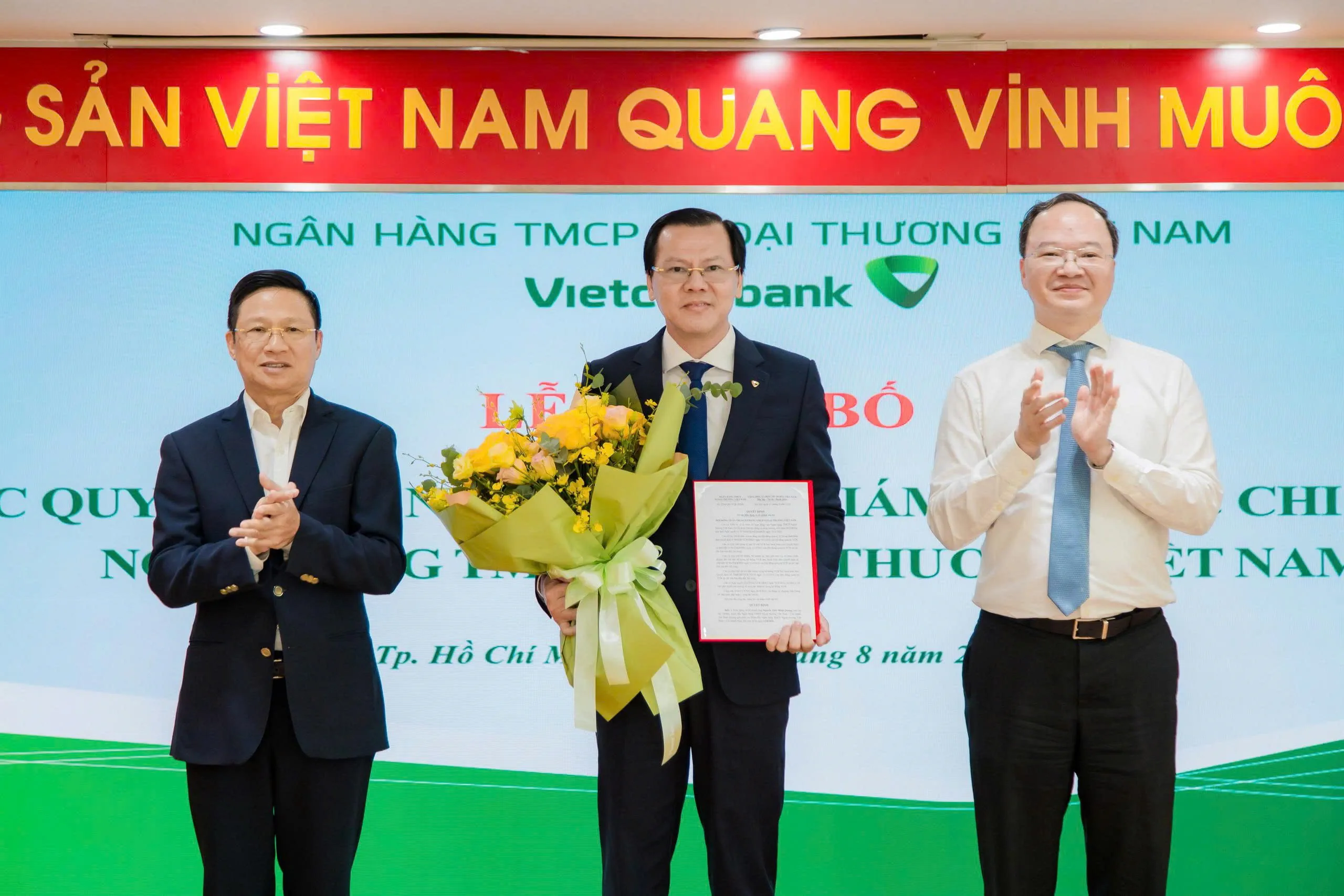 Ông Võ Minh Tuấn - Giám đốc Ngân hàng Nhà nước Khu vực 2 (bên trái) cùng ông Lê Quang Vinh - Thành viên HĐQT, Tổng Giám đốc Vietcombank (bên phải) trao quyết định và tặng hoa chúc mừng ông Nguyễn Thái Minh Quang - tân Giám đốc Vietcombank Nam Sài Gòn