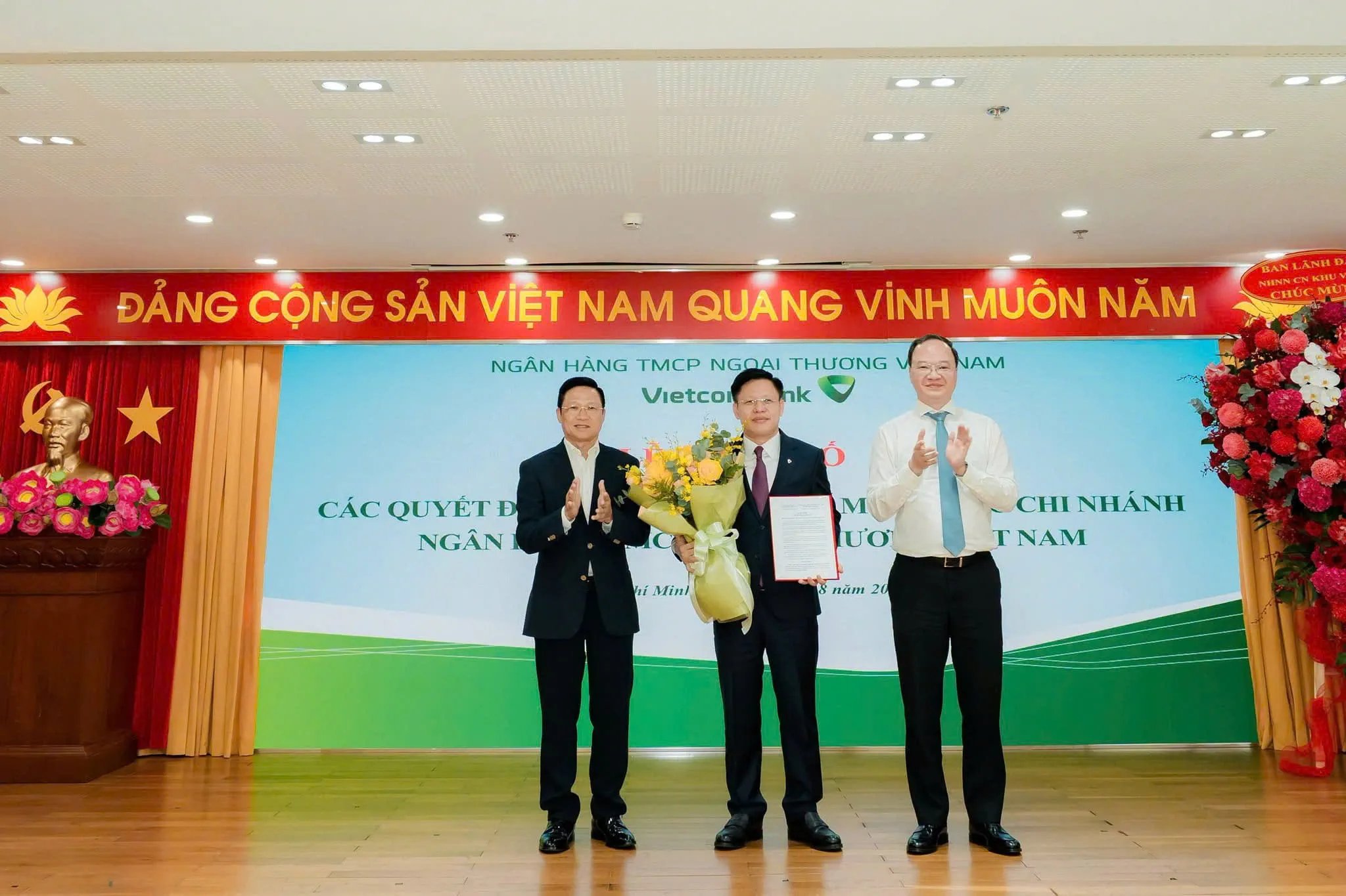 Ông Võ Minh Tuấn - Giám đốc Ngân hàng Nhà nước Khu vực 2 (bên trái) cùng ông Lê Quang Vinh - Thành viên HĐQT, Tổng Giám đốc Vietcombank (bên phải) trao quyết định và tặng hoa chúc mừng ông Ngô Minh Nhựt - tân Giám đốc Vietcombank TP. Hồ Chí Minh